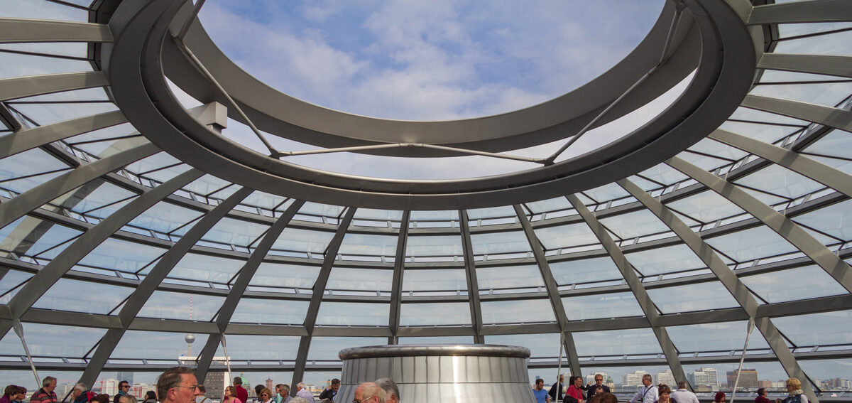 Blick von innen in die gläserne Kuppel des Reichstagsgebäudes mit ihrer Stahl-Glas-Konstruktion und der offenen Deckenöffnung.